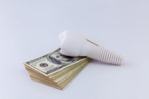 Model implant and money representing the cost of dental implants in Belmont